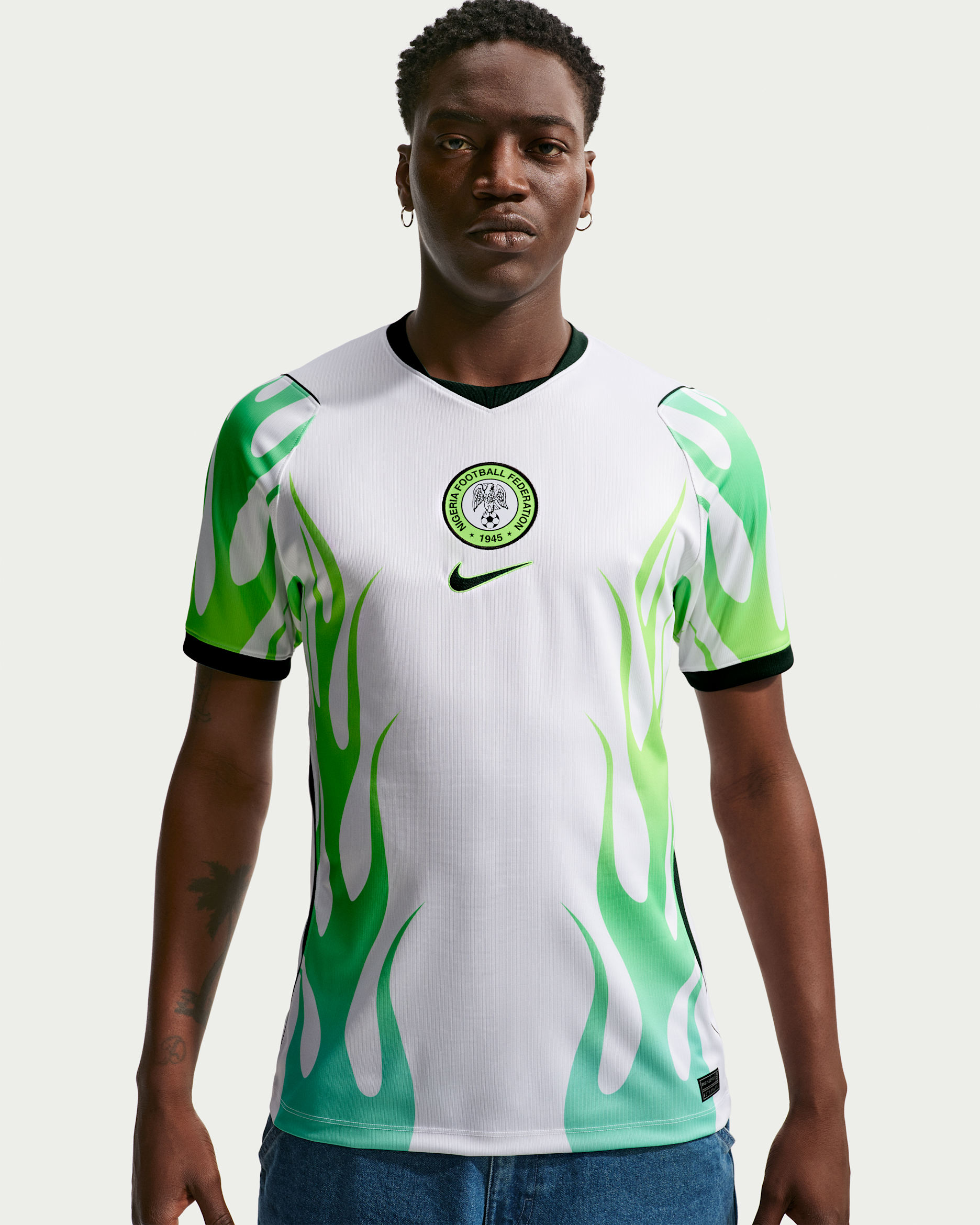 A male model wearing the 2026 Nike Super Eagles away jersey, featuring a white base with green flame patterns rising from the hem.