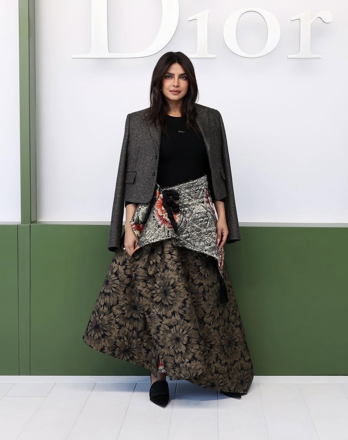 Priyanka Chopra is wearing a grey blazer over a voluminous floral skirt with orange accents at the Dior Autumn/Winter 2026 show during Paris Fashion Week — Paris Fashion Week celebrity styles