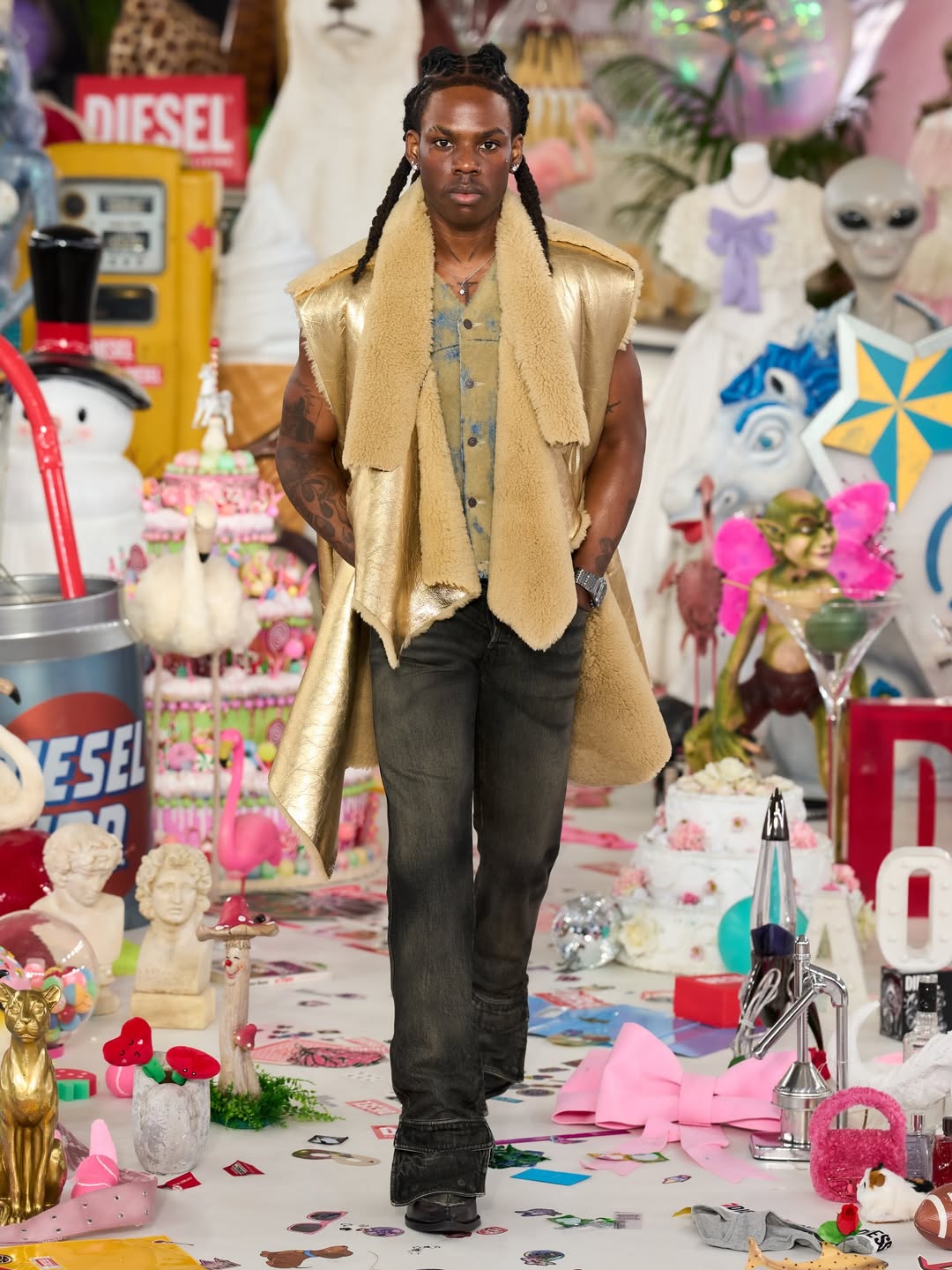 Rema walking the runway for Diesel Fall/Winter 2026 at Milan Fashion Week, wearing a metallic gold shearling vest and dark distressed denim.