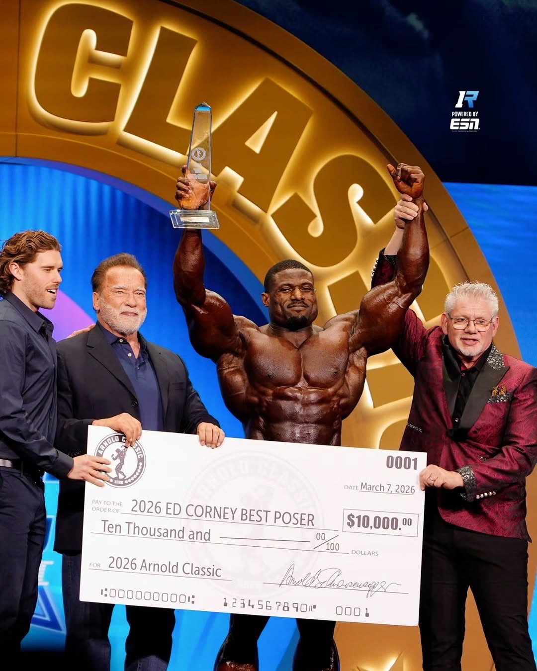 Chinedu Andrew Obiekea (Andrew Jacked) holding his 2026 Arnold Classic trophy and grand prize check alongside Arnold Schwarzenegger.