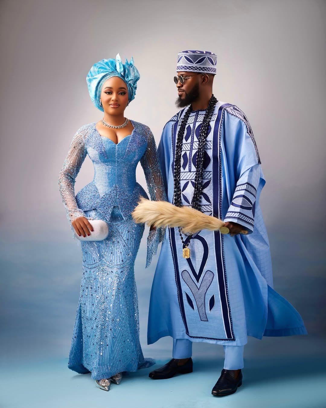 Akin Faminu in a powder blue agbada with navy embroidery standing next to Kiky Festus in a crystal-embellished powder blue mermaid gown at a traditional wedding.