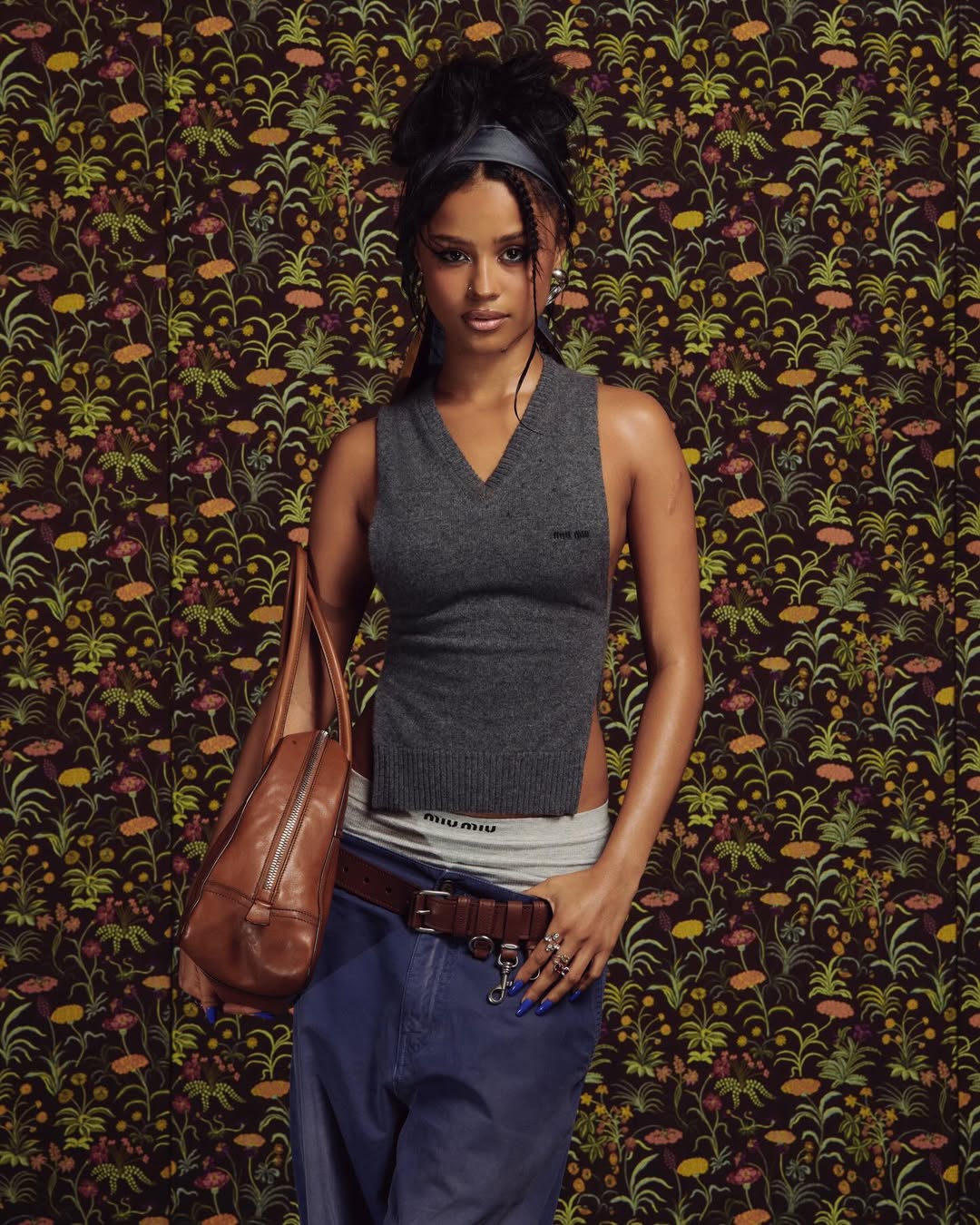 Tyla at the Miu Miu Fall/Winter 2026 show in Paris wearing a grey open-side knit vest and low-slung blue jeans that reveal the logo waistband of grey Miu Miu briefs.