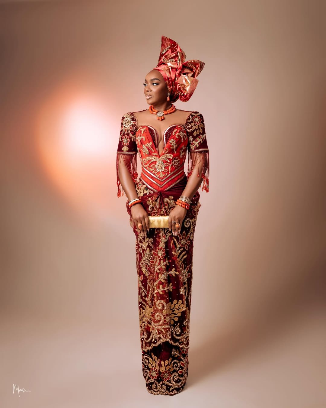 Chioma Akpotha posing in a custom wine-toned beaded gown and traditional coral accessories for her birthday celebration.