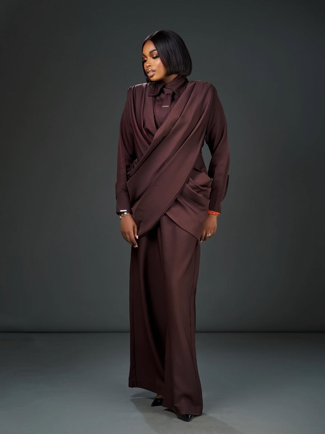 A full-length portrait of Sabrina Idukpaye in a sculptural chocolate brown co-ord set with traditional coral beads.