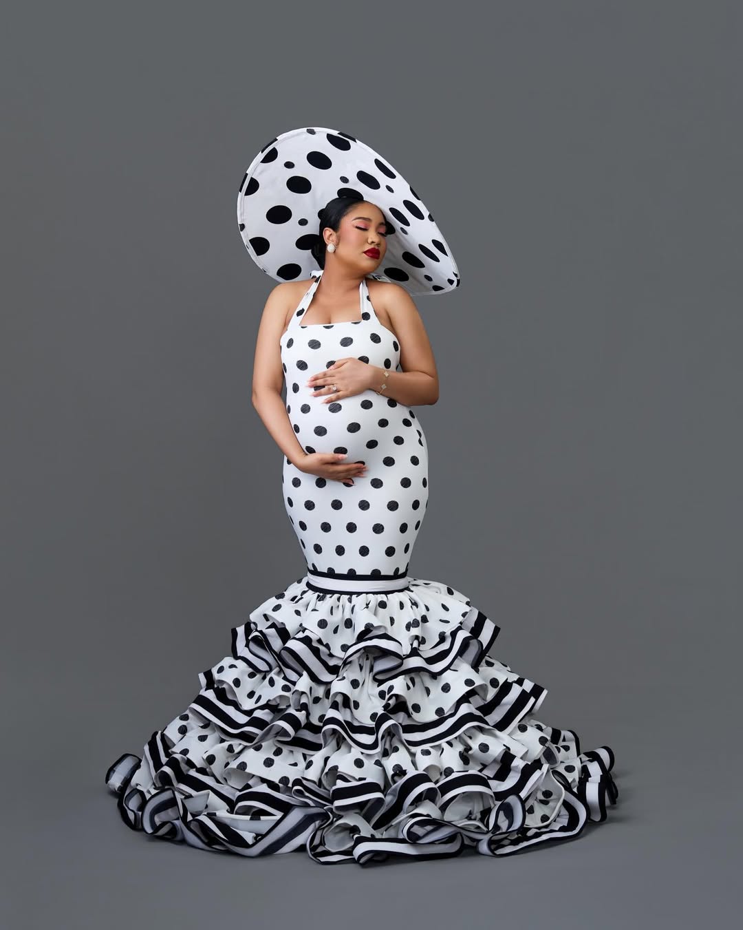 Anna Ebiere Banner in a black and white polka-dot halter gown with a matching oversized disc hat, showcasing her baby bump.