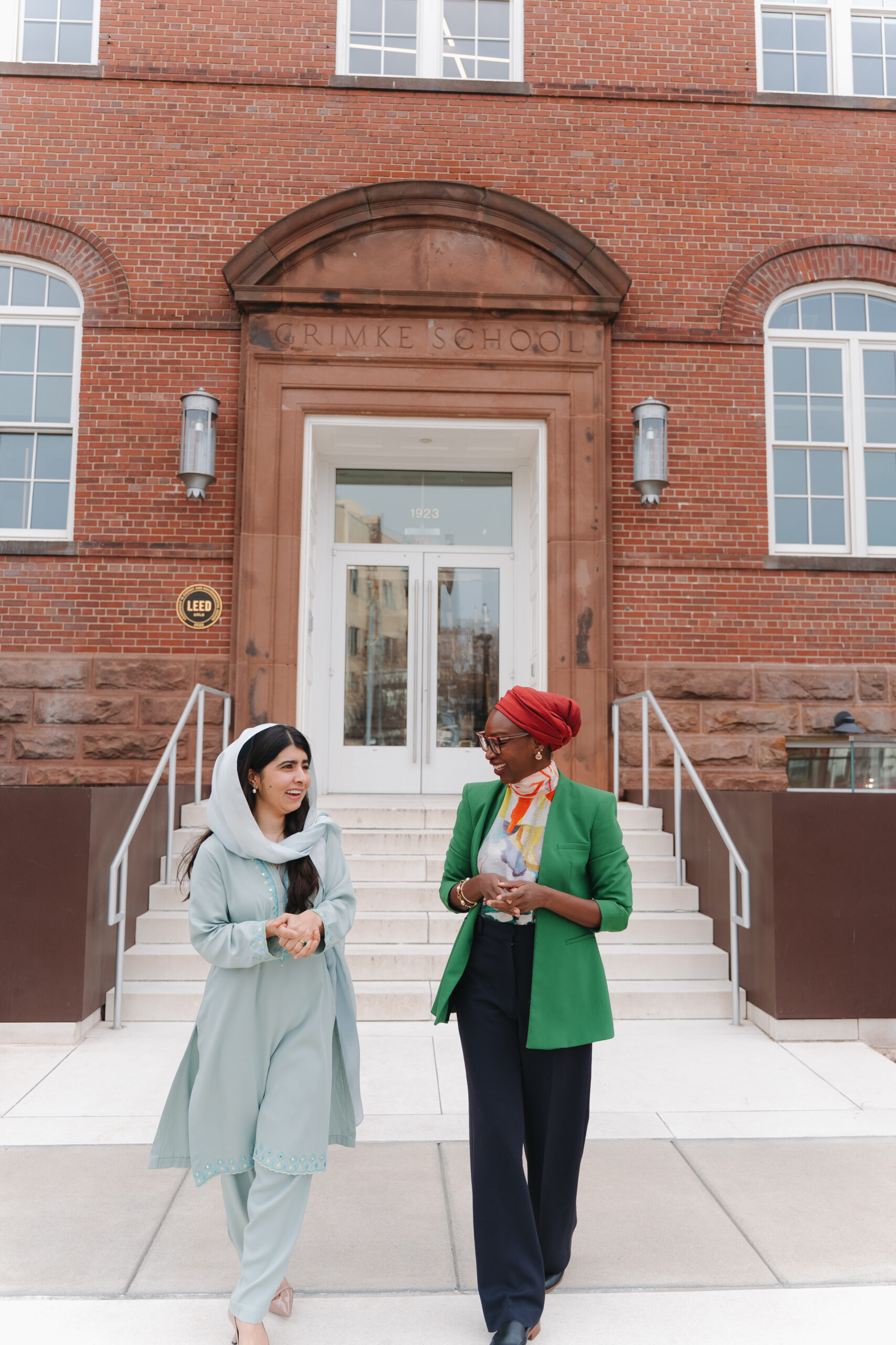 Malala Fund CEO Nabila Aguele and co-founder Malala Yousafzai walking and talking outside the historic Grimke School building.