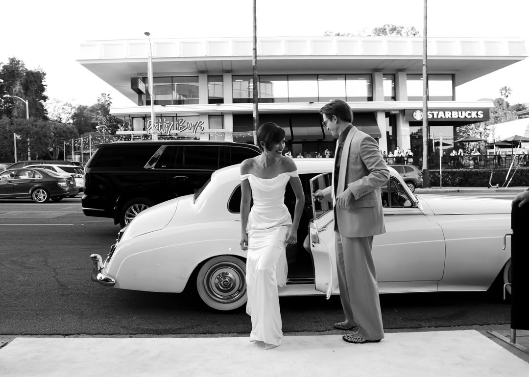 lack and white candid photo of Zendaya in a vintage Vivienne Westwood bridal gown stepping out of a classic car with co-star Robert Pattinson.