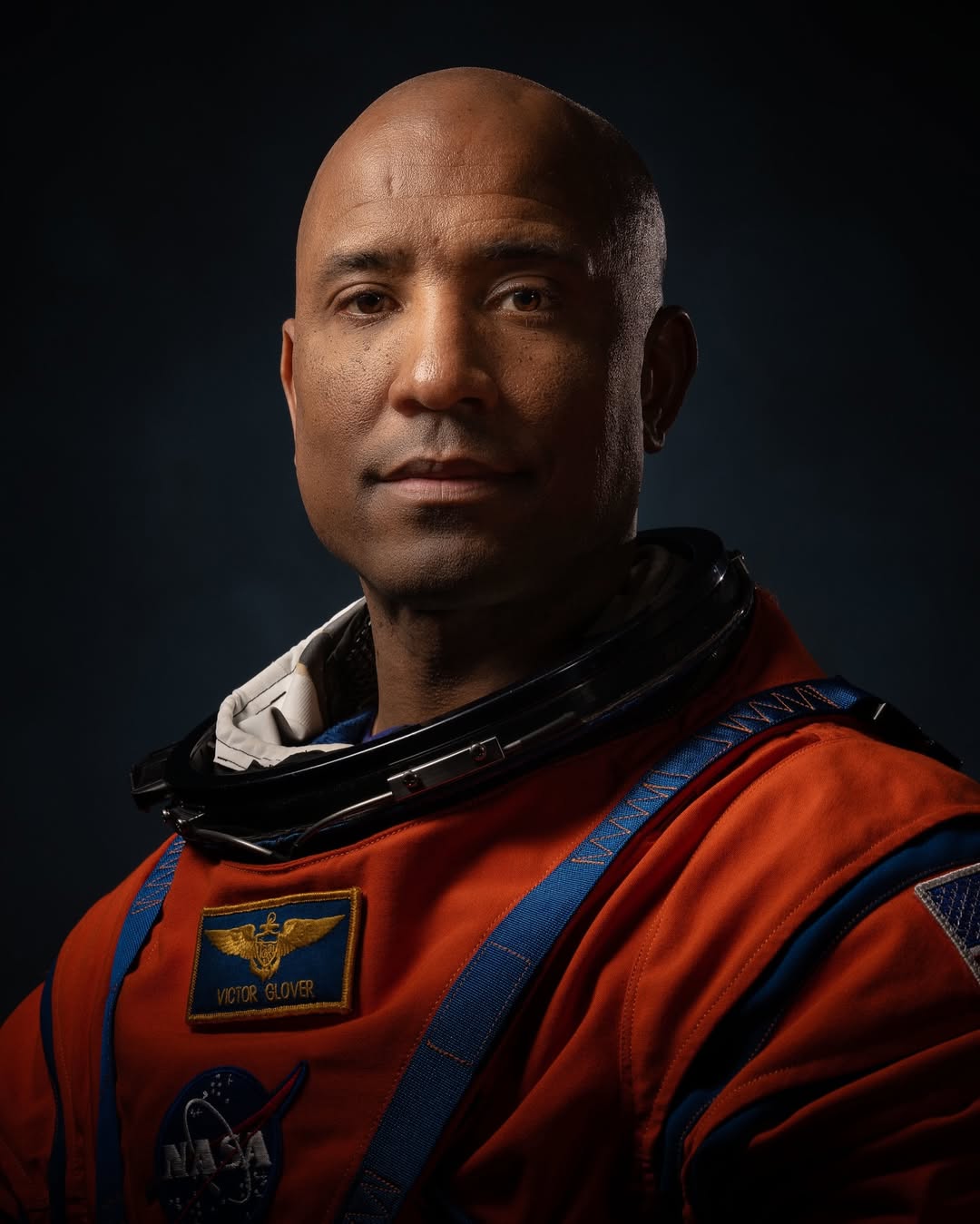 Artemis II Pilot Victor Glover in an orange NASA flight suit with blue neck trim and a name patch.