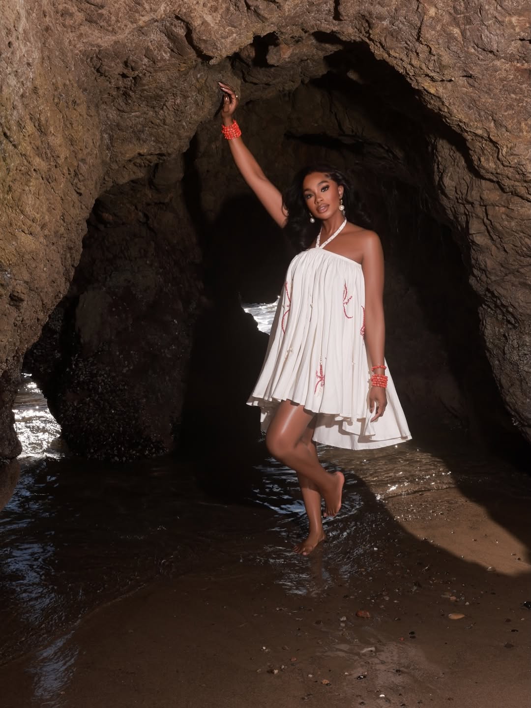Sharon Ooja Nwoke posing in a sea cave wearing a white halter dress by Knanfe for her 2026 birthday photoshoot.