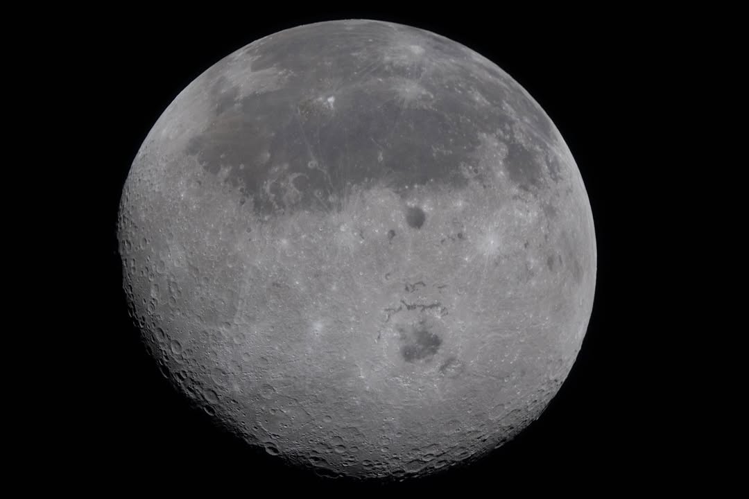 A full view of the Moon showing the dark lava flows of the near side and the cratered far side, with the Orientale Basin in the centre.