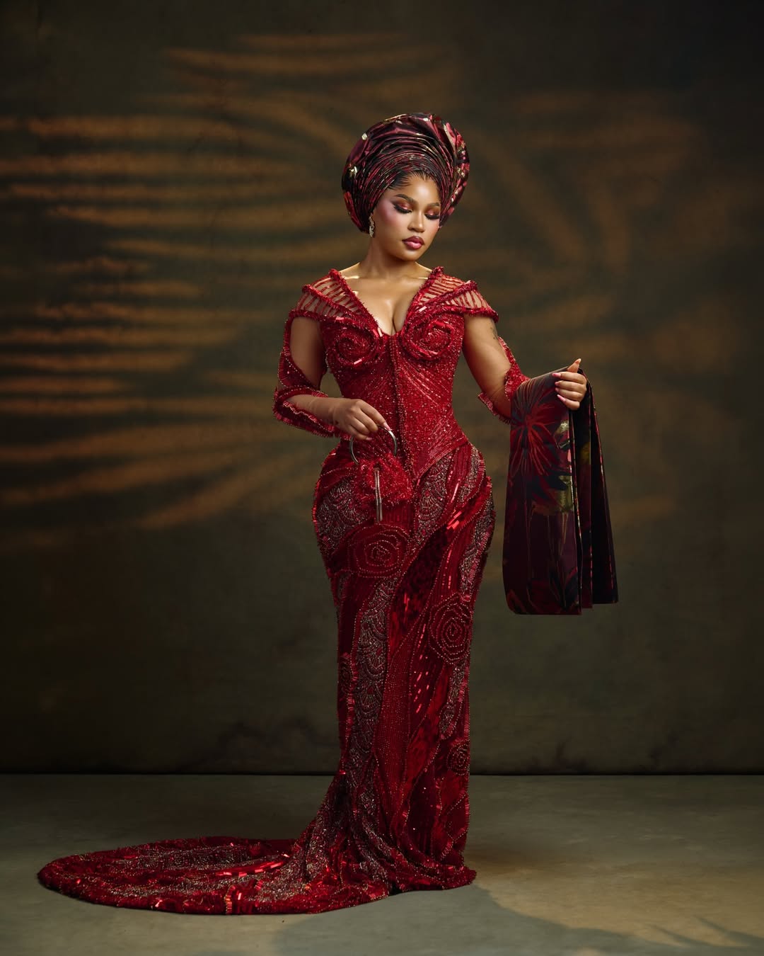 Adeola C Adeyemi (Diiadem) in a deep crimson red embellished mermaid gown by Emagine By Bukola, styled with a structured gele and matching striped ipele.