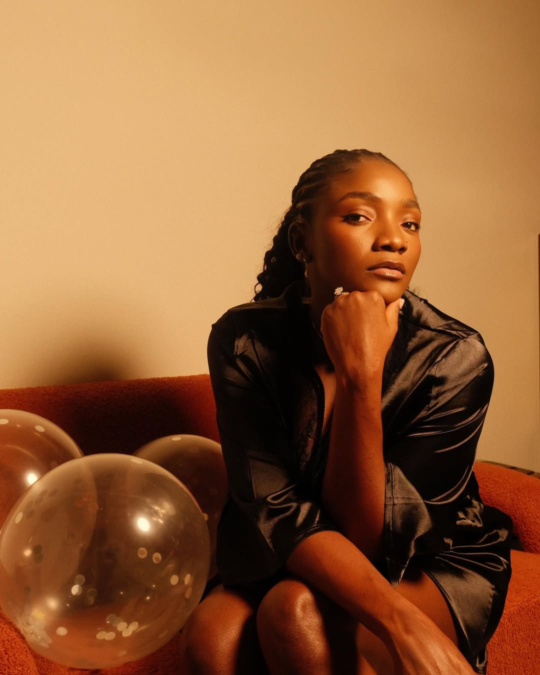 A close-up portrait of Simi resting her chin on her hand, posing on a couch next to confetti balloons during her 38th birthday celebration.