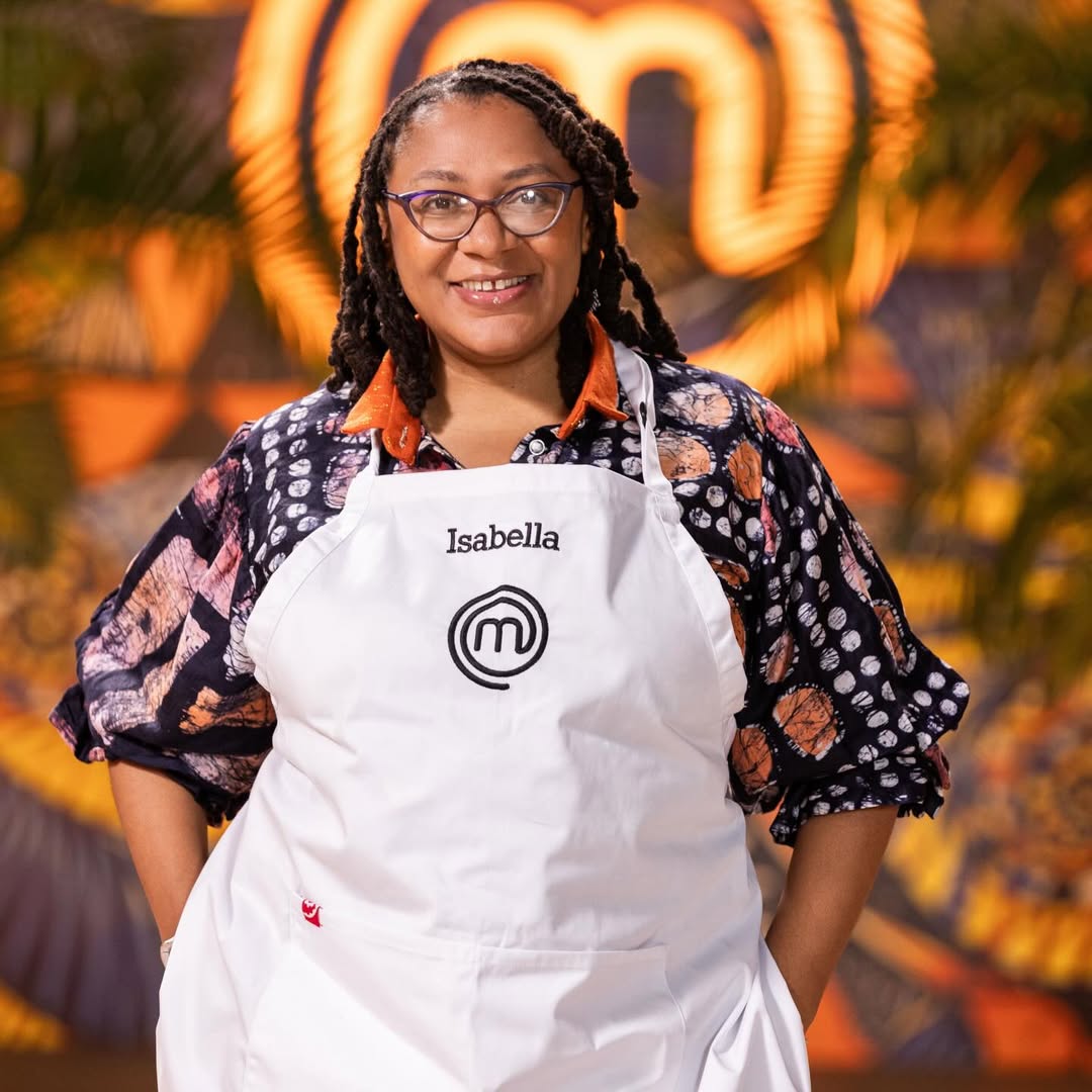 MasterChef Nigeria contestant Isabella Adediji smiling with hands in pockets, wearing an adire patterned shirt beneath her apron