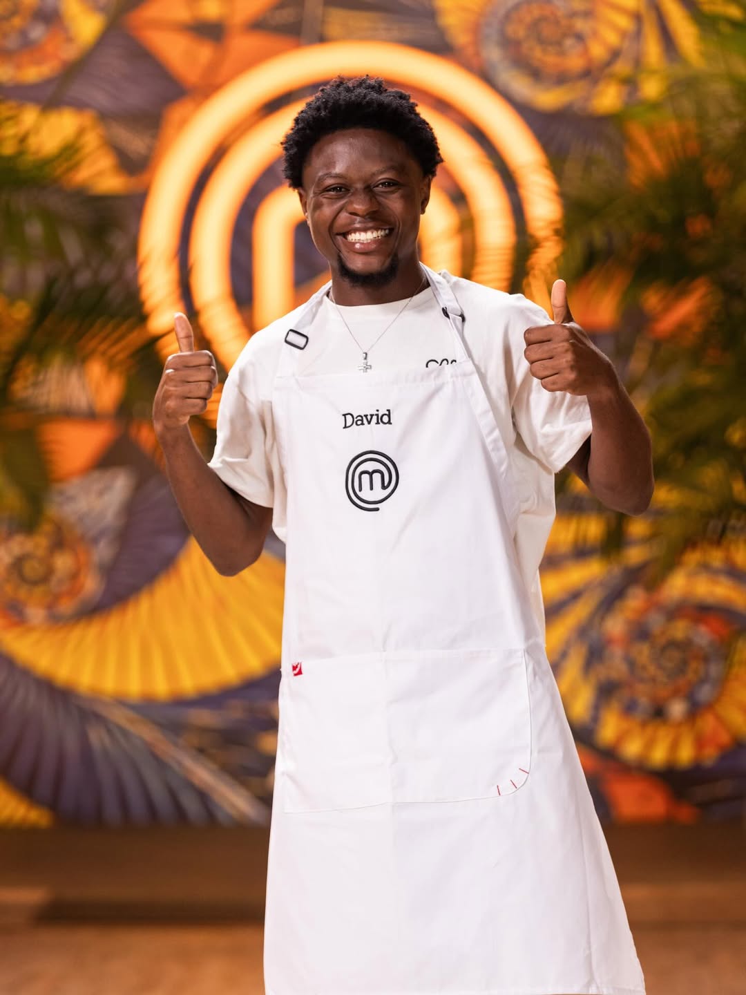 MasterChef Nigeria contestant David Emmanuel smiling broadly and giving two thumbs up while wearing his apron.