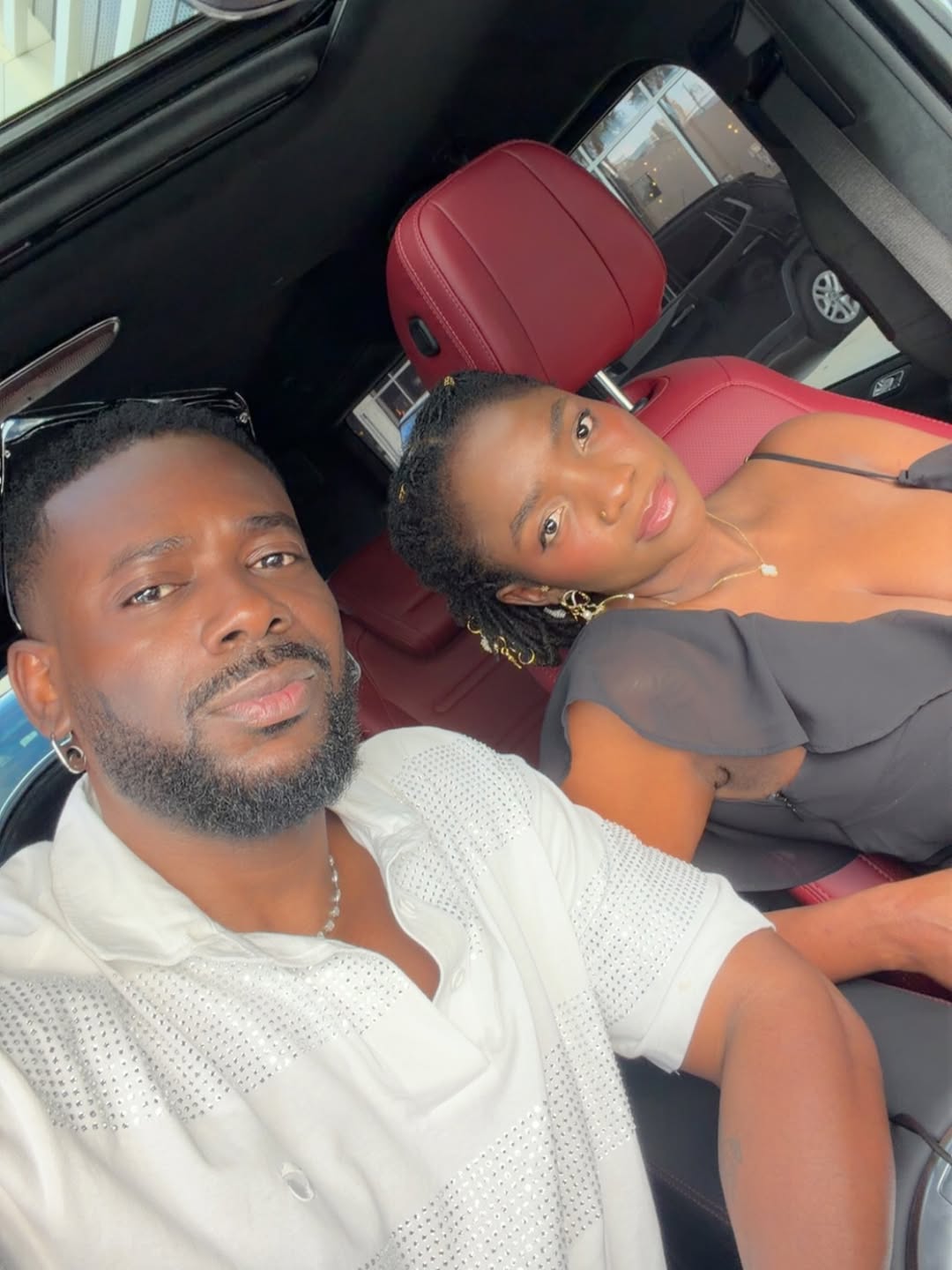 A close-up of Adekunle Gold and Simi sitting together in the back of a car during her 38th birthday celebrations. Adekunle is leaning in towards Simi, who is wearing a black dress and silver jewellery.