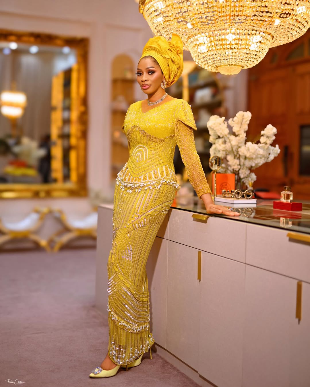 A full-length portrait of Shade Okoya on her 49th birthday, wearing a mustard gold embellished floor-length gown by Tubobereni and a sculptural yellow gele.