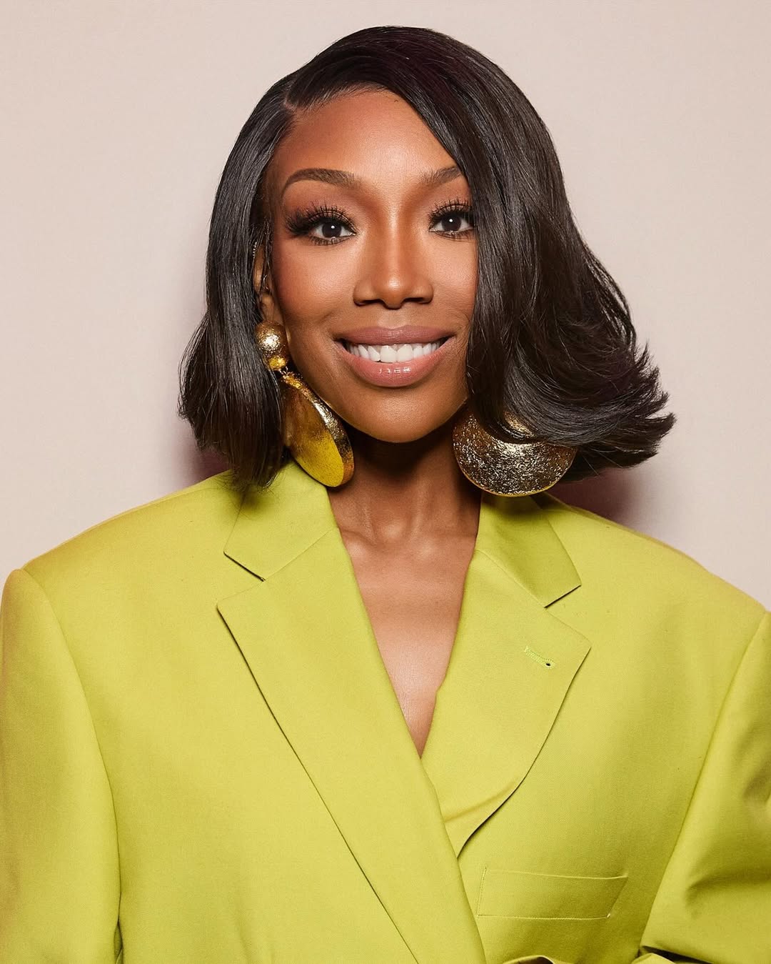 Close-up portrait of Brandy’s beauty look for The Jennifer Hudson Show, featuring a sleek chin-length bob with flicked ends and massive hammered-gold disc earrings.