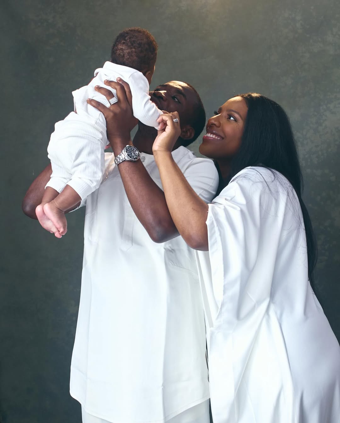 Theophilus Sunday and Ashlee Sunday holding their son Mystery during a family photo session in all-white outfits.