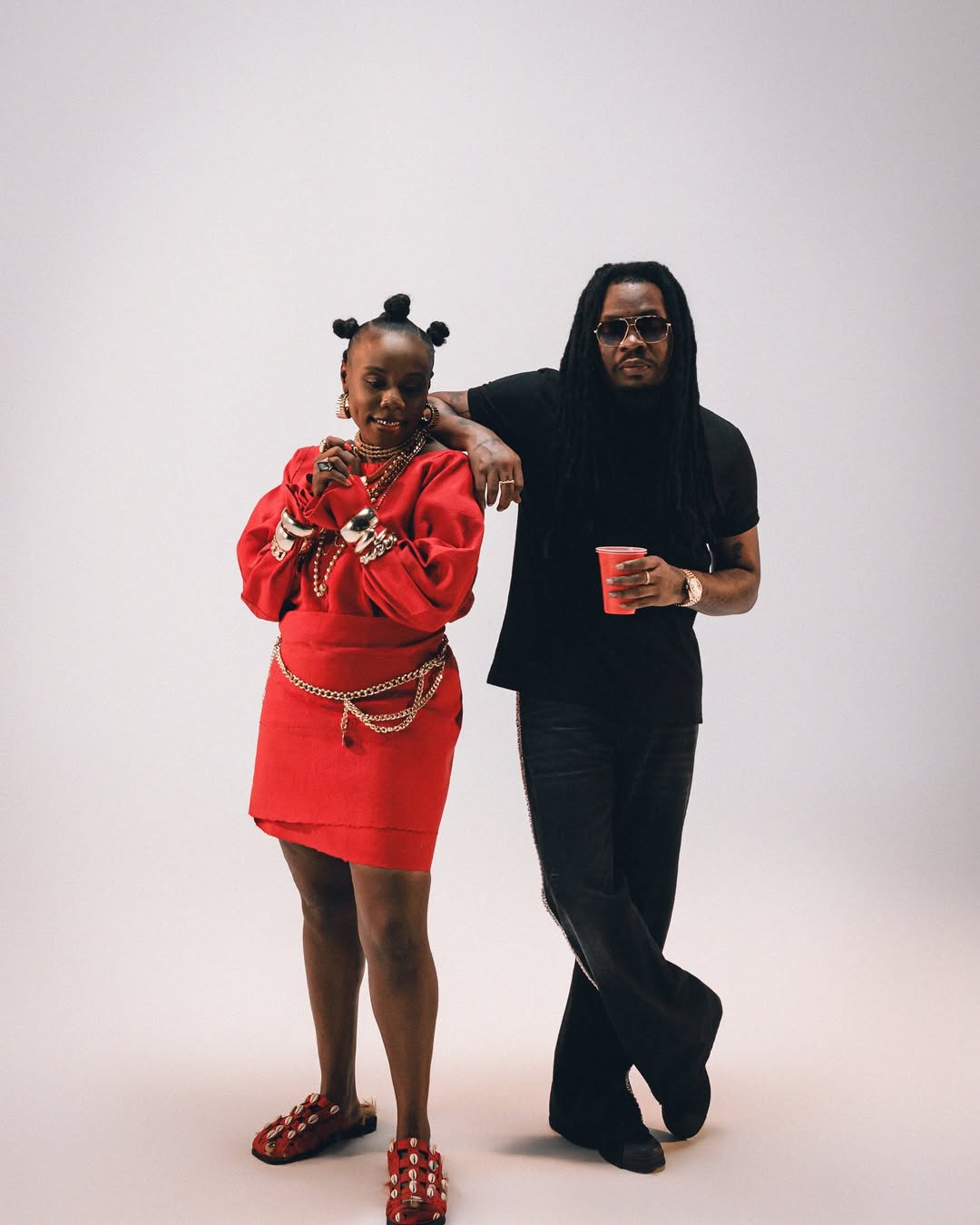 Teni-the-Entertainer wearing a red-monochromatic-outfit with cowrie-shell-sandals and Olamide in all-black-streetwear for the Zion music video.