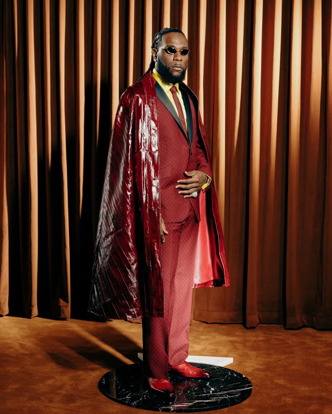 Burna Boy wearing a custom burgundy suit and leather cape by Ozwald Boateng at the 2025 Met Gala.