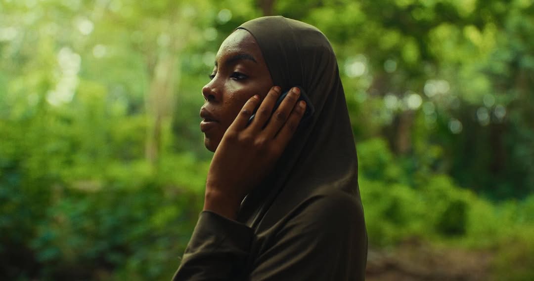 Amal Umar as a member of the bandits' camp in the crime thriller The Herd, wearing a dark hijab while speaking on a mobile phone.
