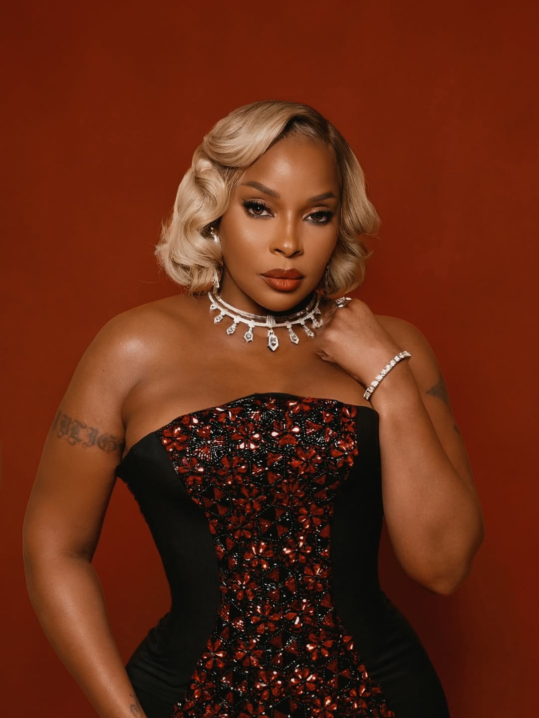 Mary-J-Blige-wearing-a-black-strapless-gown-with-red-floral-embellishments and a silver-diamond-fringe-choker.