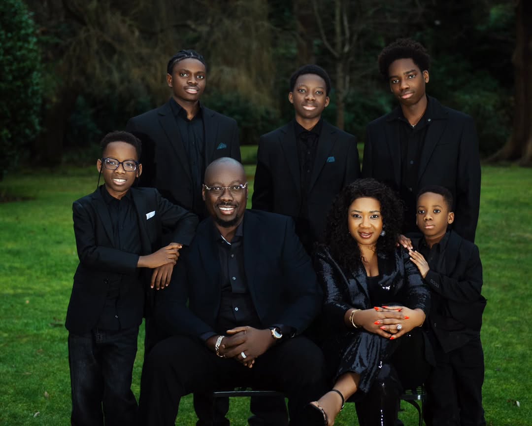 Close-up portrait of Obi Cubana and Ebele Iyiegbu seated with their five sons in coordinated black formal wear for a family photoshoot.