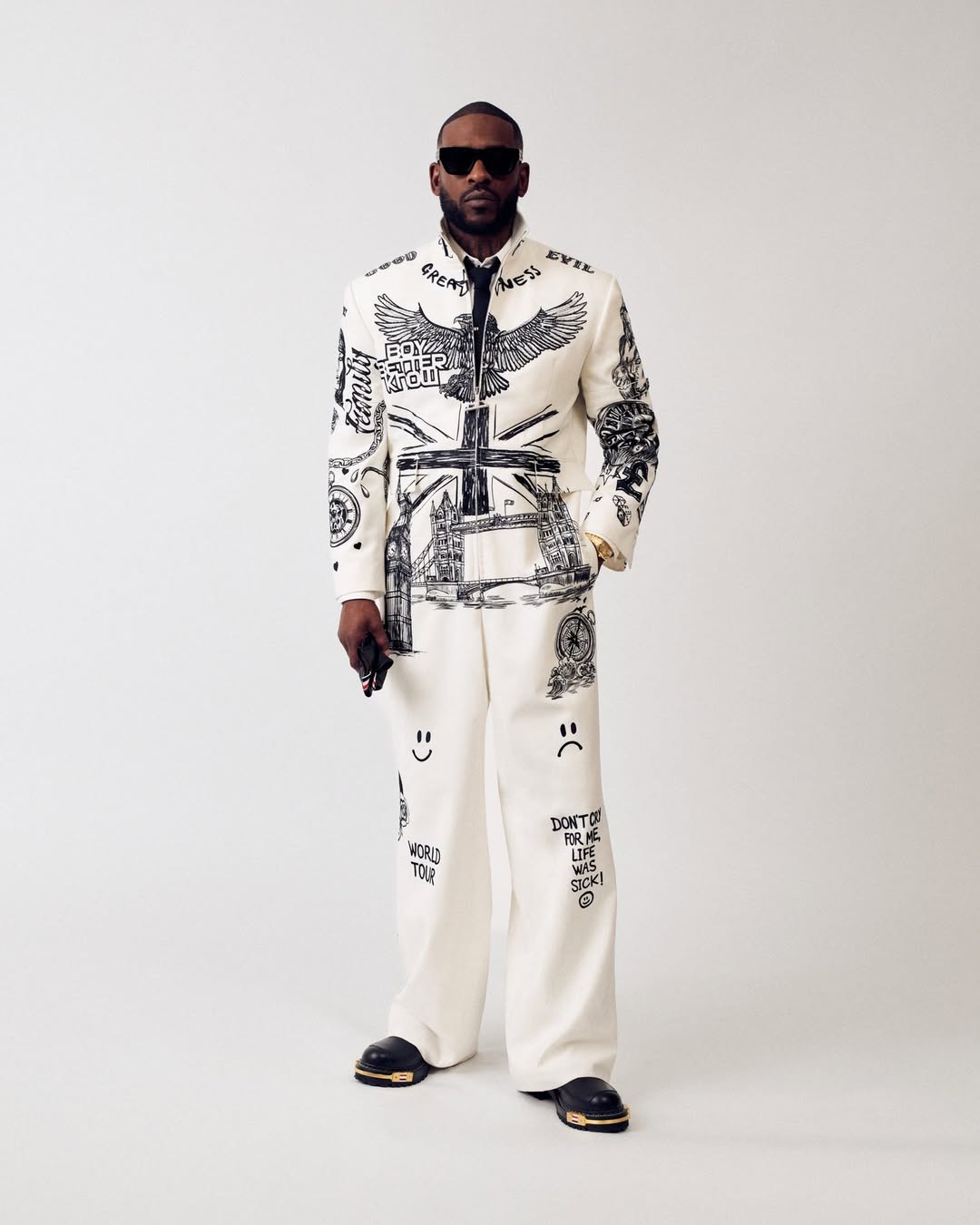 Skepta wearing a custom white wool Thom Browne tailored jumpsuit featuring black satin stitch embroidery of his personal tattoo art at the 2026 Met Gala.