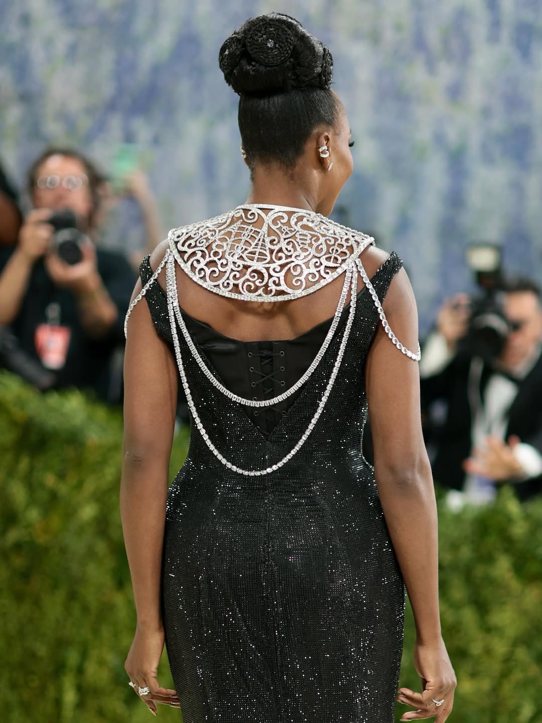 Back view of Venus Williams at the 2026 Met Gala showing the Swarovski silver filigree collar neckpiece and cascading crystal chains over her black sequin gown with a corset back detail and high braided updo by JAWARA