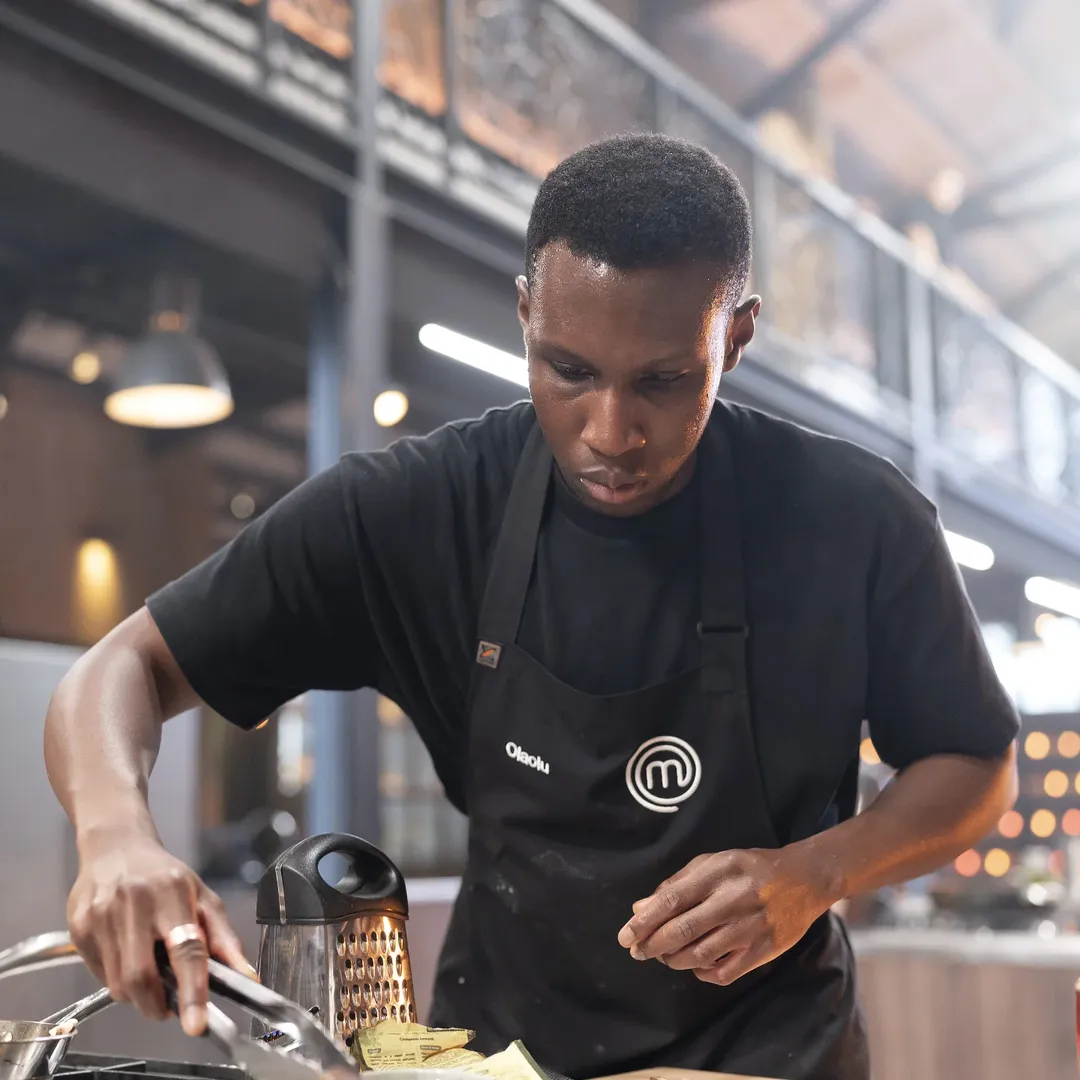 Olaolu Olorunnimbe cooking in the MasterChef Australia kitchen during the 2026 auditions, preparing his signature West African heritage dish.