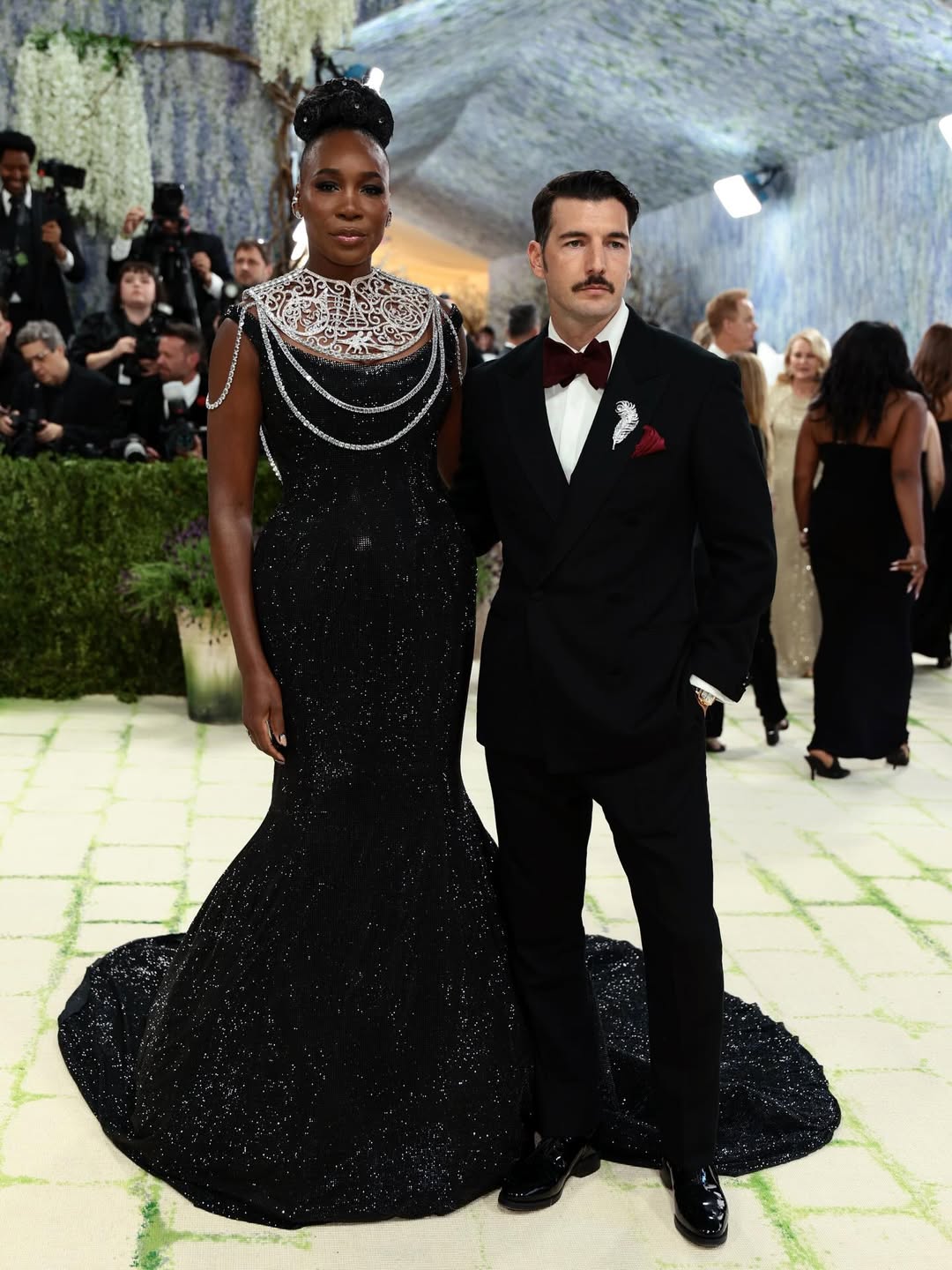 Venus Williams and husband Andrea Preti at the 2026 Met Gala, Venus in a black Swarovski sequin gown and Andrea in a black tuxedo with burgundy bow tie and silver feather brooch