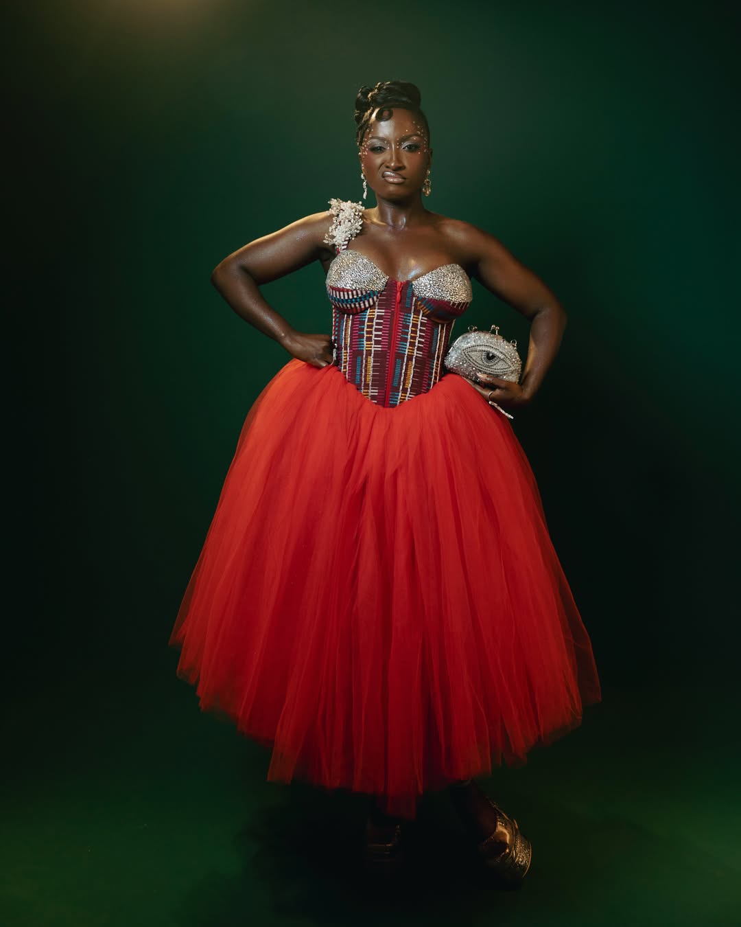 Genoveva Umeh posing in her custom Sòró Asò AMVCA 2026 dress featuring an Akwaete fabric corset and red tulle skirt.