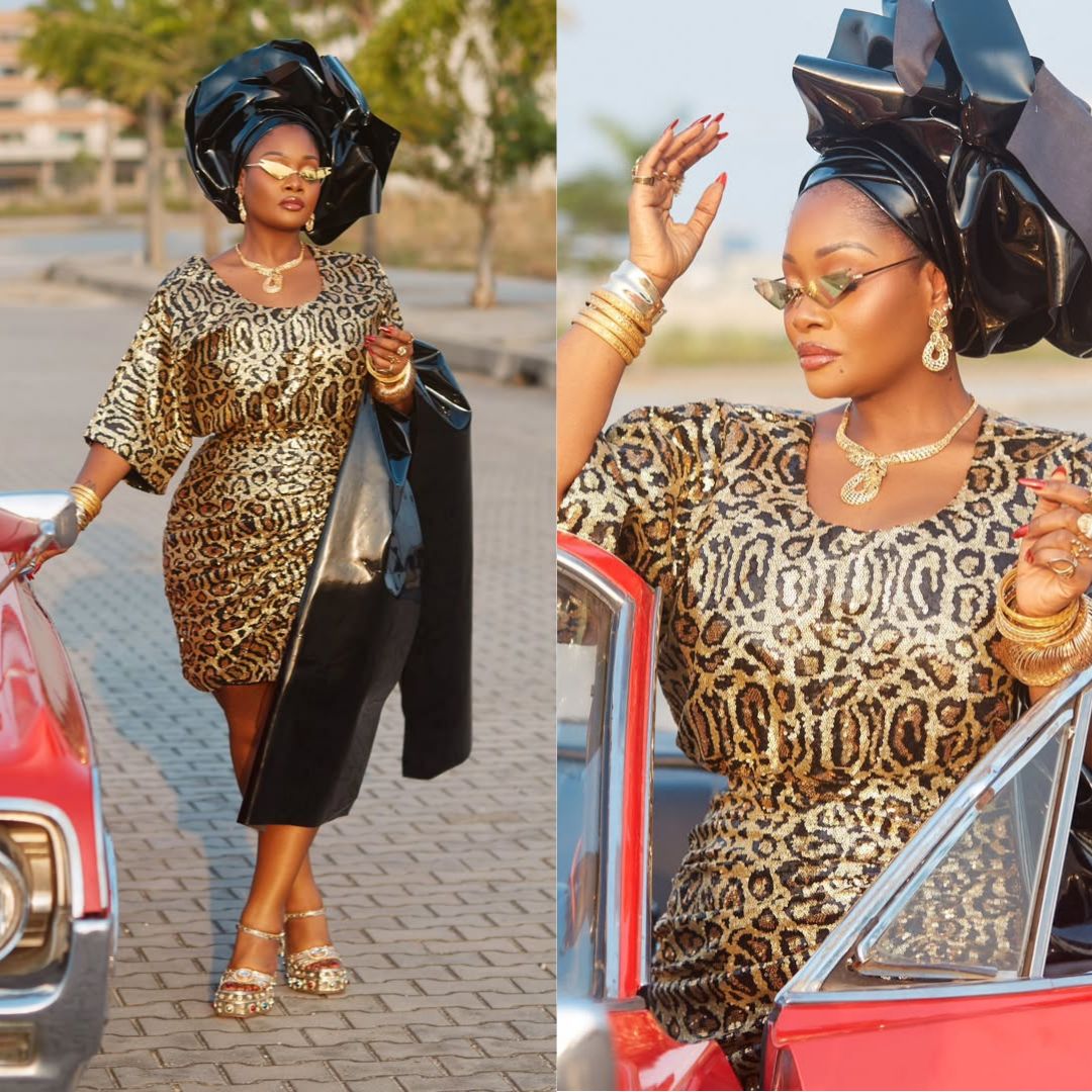 Toolz Oniru-Demuren in a gold and black leopard-print Oleku outfit paired with a glossy black leather gele and futuristic gold sunglasses by a vintage car.