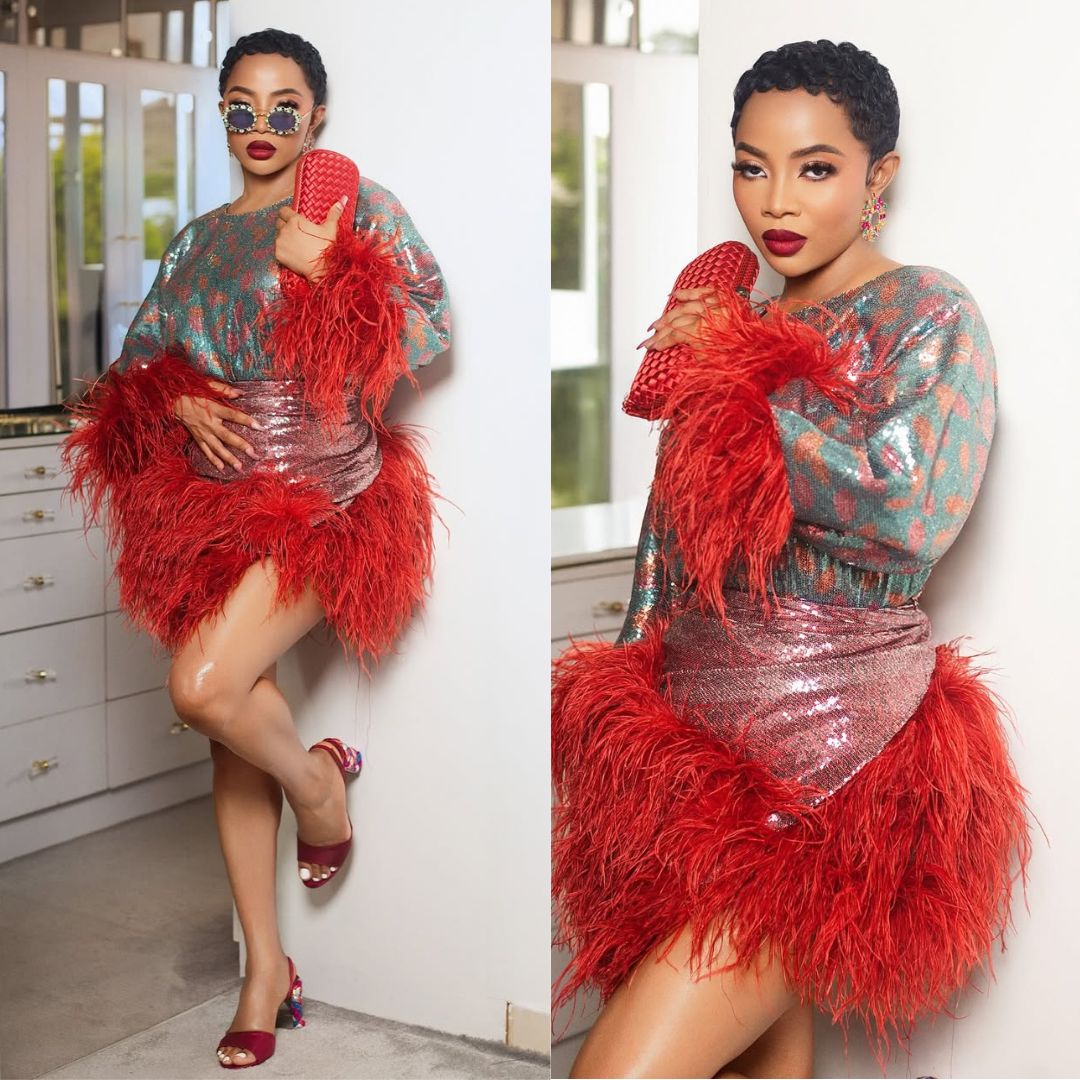 Media personality Toke Makinwa leaning against a wall wearing a multi-coloured sequinned Oleku style by Wanni Fuga, featuring dramatic red feathers.