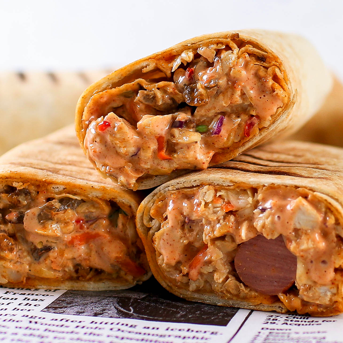 Three toasted Nigerian beef shawarma wraps by Kikifoodies sliced in half, showing a rich mixture of beef, cabbage, carrots, and creamy pink sauce.
