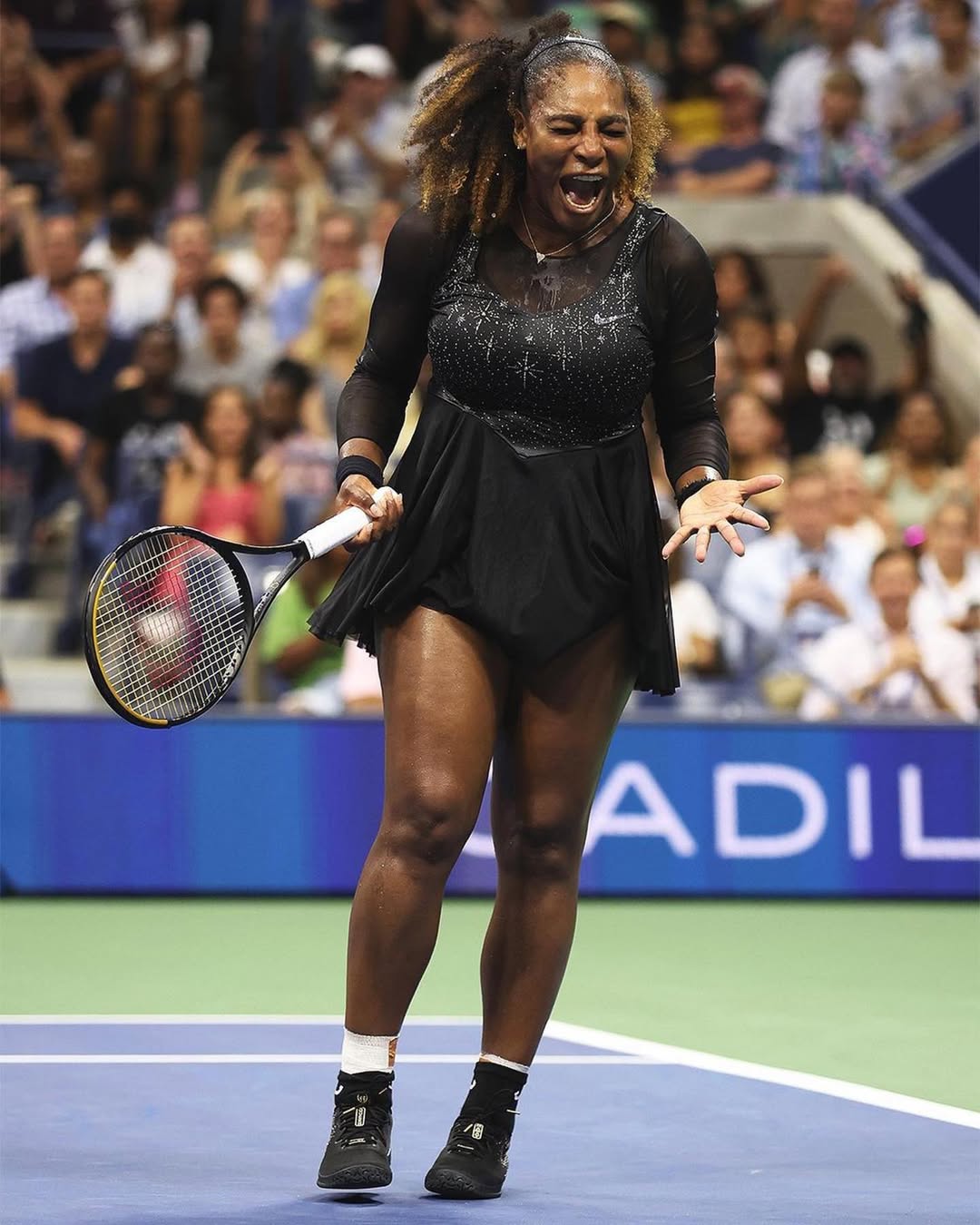 Serena Williams celebrating a point on court during the 2022 US Open, wearing her custom black sparkling tournament dress.