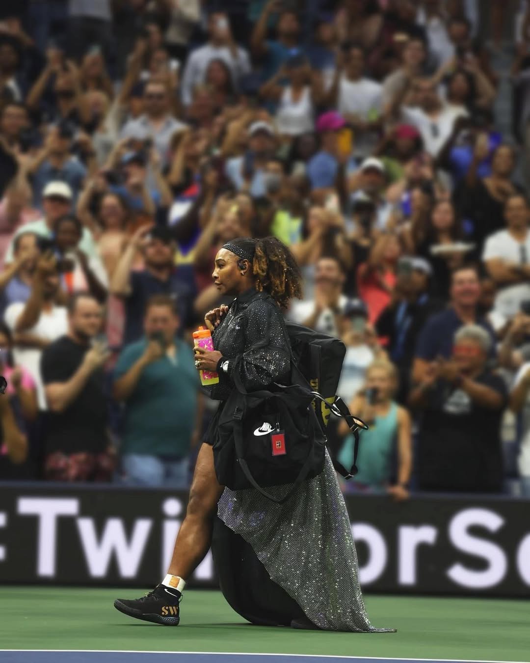Serena Williams walking off the court carrying a sports bag as a stadium crowd stands and cheers at the 2022 US Open.