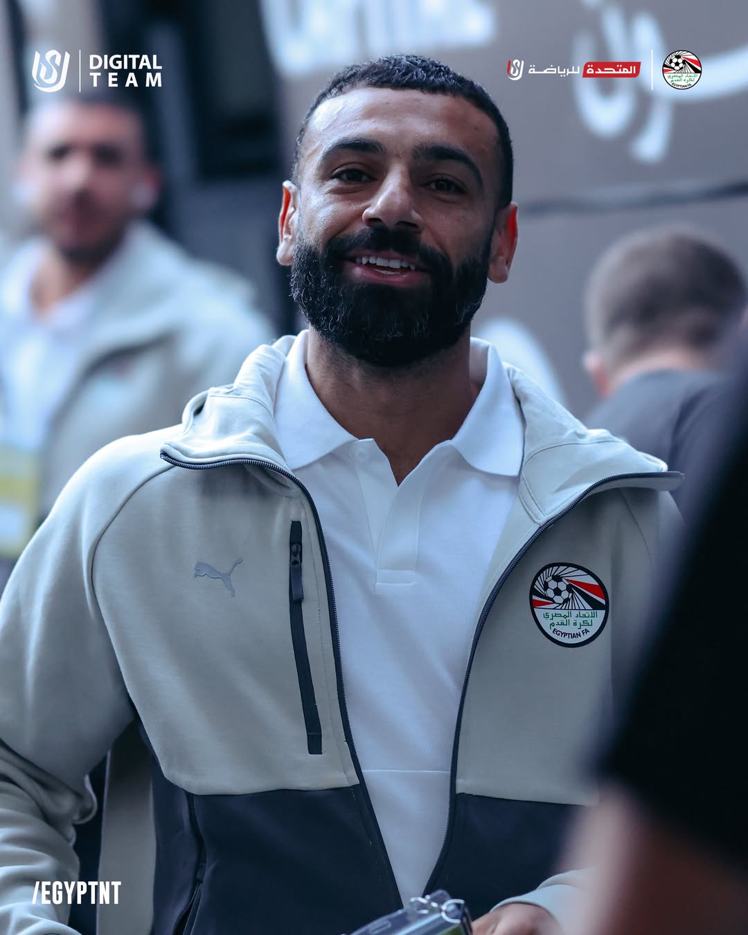 Egypt national football team captain Mohamed Salah smiling in a grey and white Puma training jacket featuring the Egyptian FA crest.