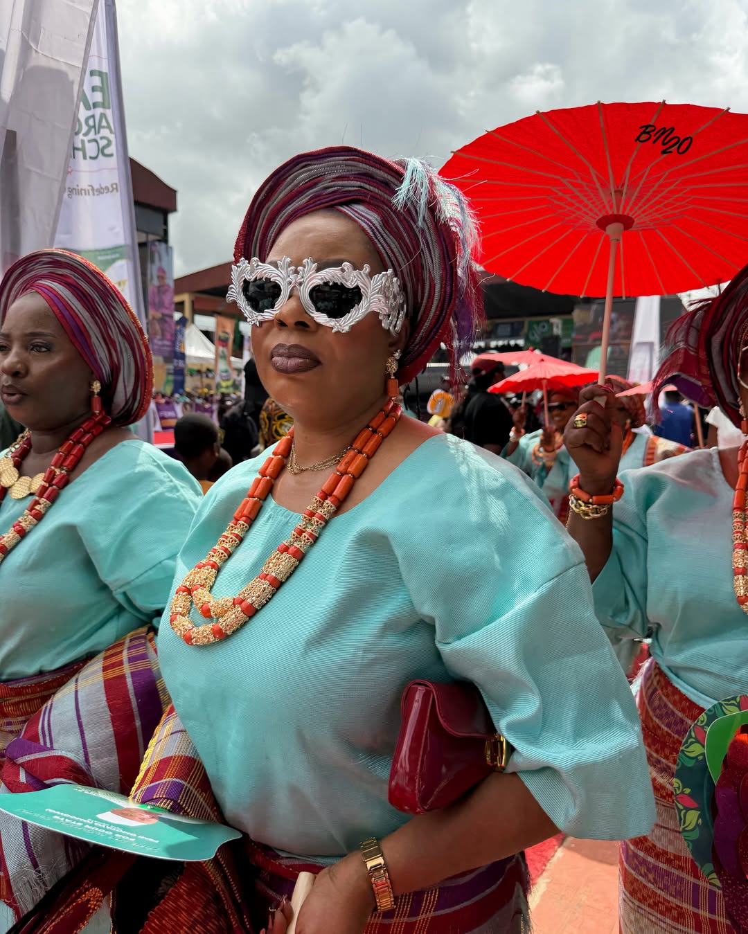 A festival attendee wearing statement sunglasses with thick, sculptural silver baroque frames, paired with a turquoise outfit 