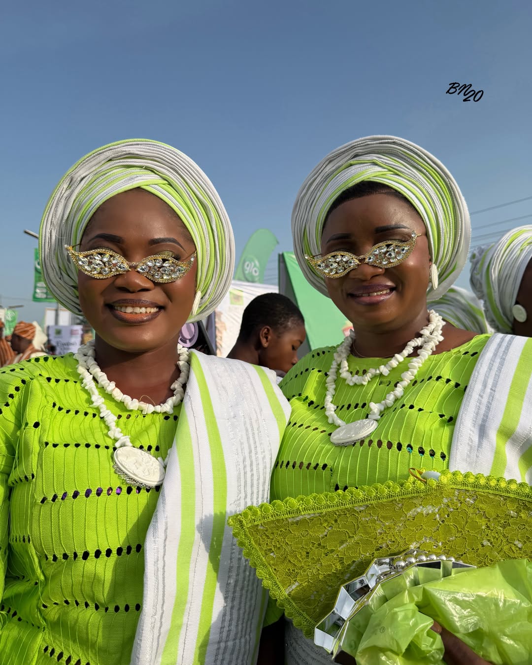 Two women in matching lime green and white striped Regberegbe attire at Ojude Oba 2026 wearing heavily crystal-bordered, wing-shaped cat-eye sunglasses.