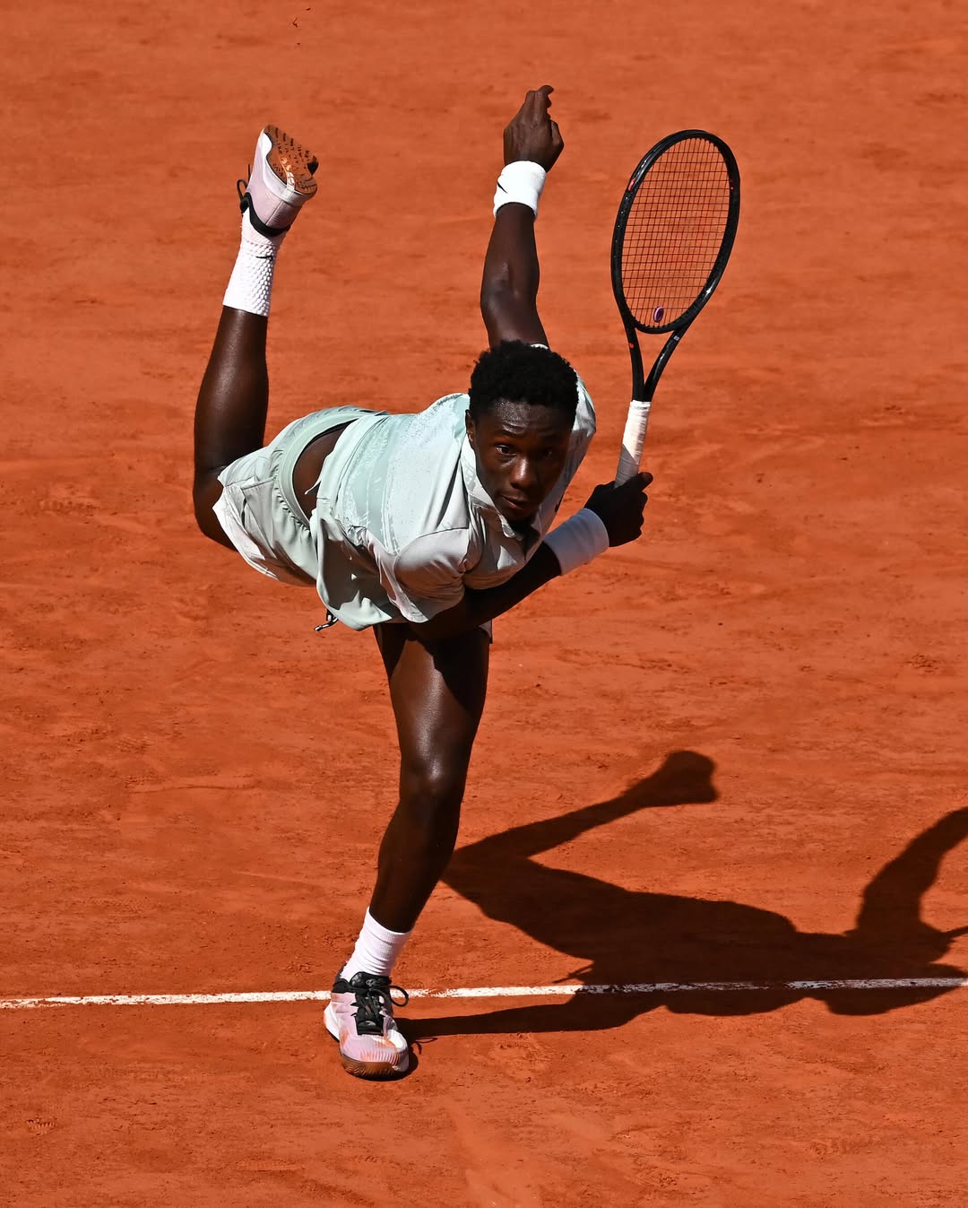 An overhead action shot of 17-year-old Moise Kouame mid-air executing a powerful serve on the red clay courts of Roland-Garros 2026.