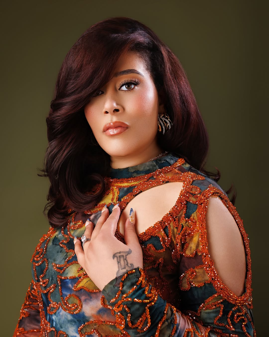 Close-up beauty headshot of Nollywood actress Adunni Ade showcasing her birthday soft glam makeup, a side-swept auburn hairstyle, and a textured abstract gown with shoulder cutouts.