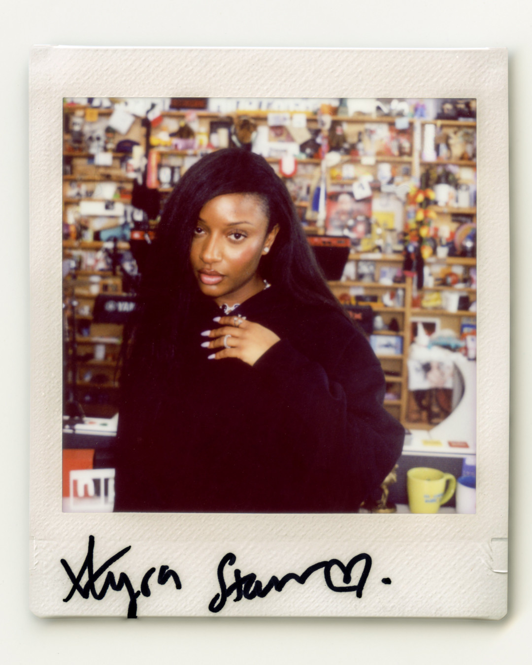 A signed Polaroid photograph of Nigerian artist Ayra Starr posing in a black hoodie at the NPR studio with her signature at the bottom.