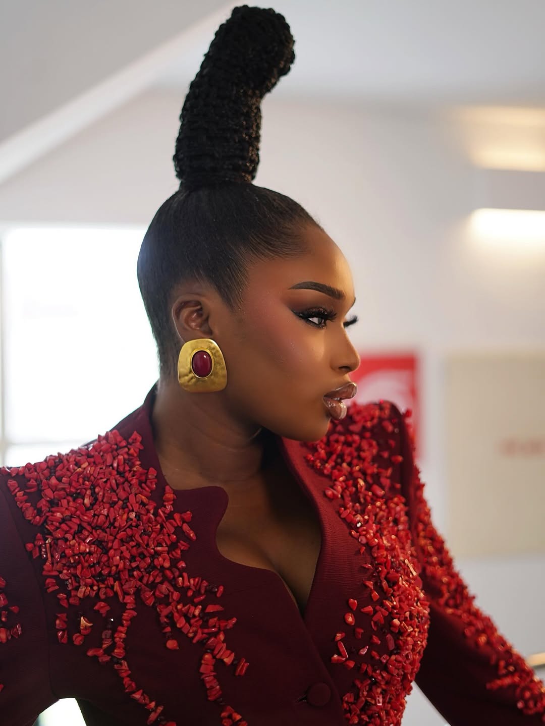 Sabrina Idukpaye showcasing her braided top knot hairstyle inspired by Benin's Queen Idia with gold statement earrings.