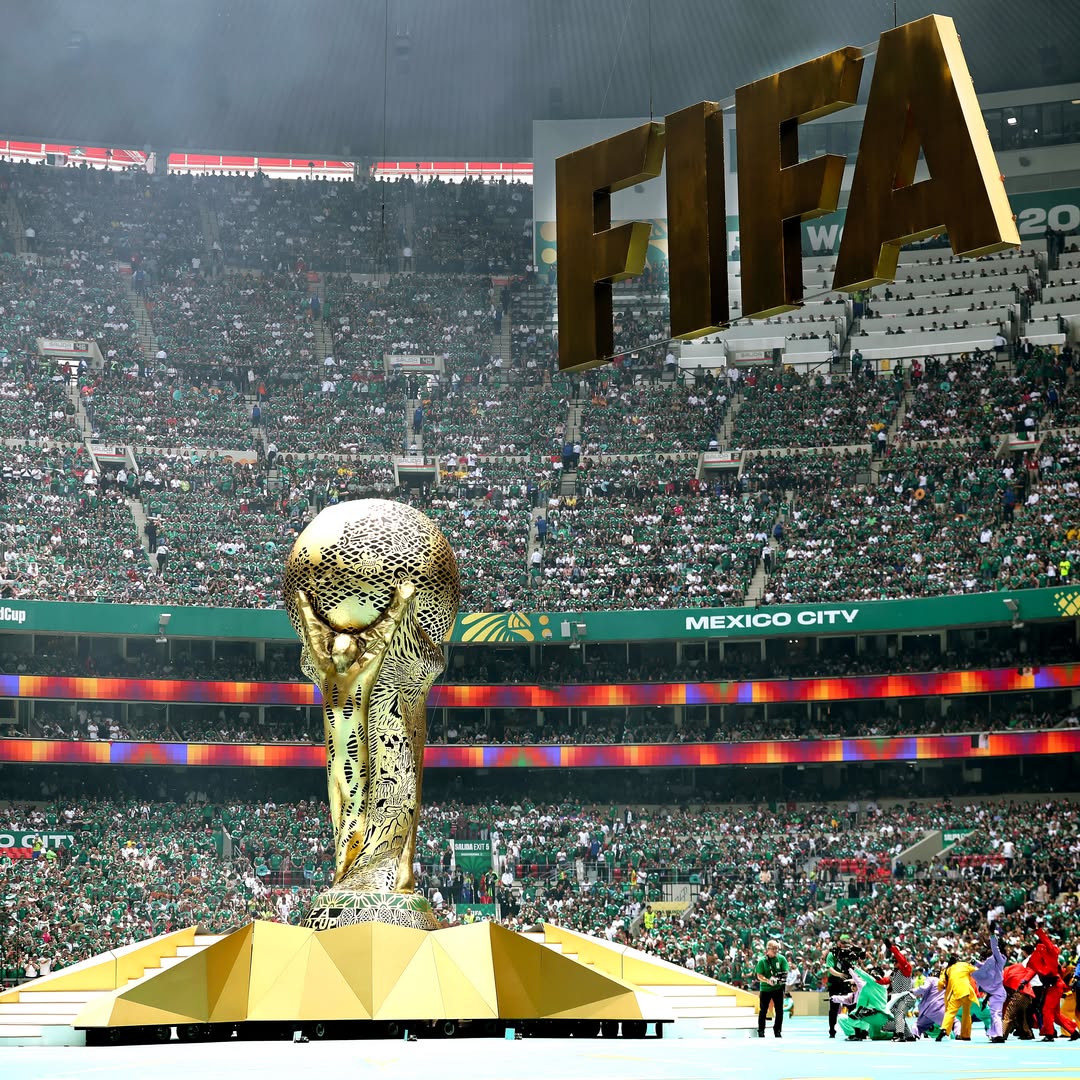 A massive gold FIFA World Cup trophy replica standing in the center of a packed stadium.