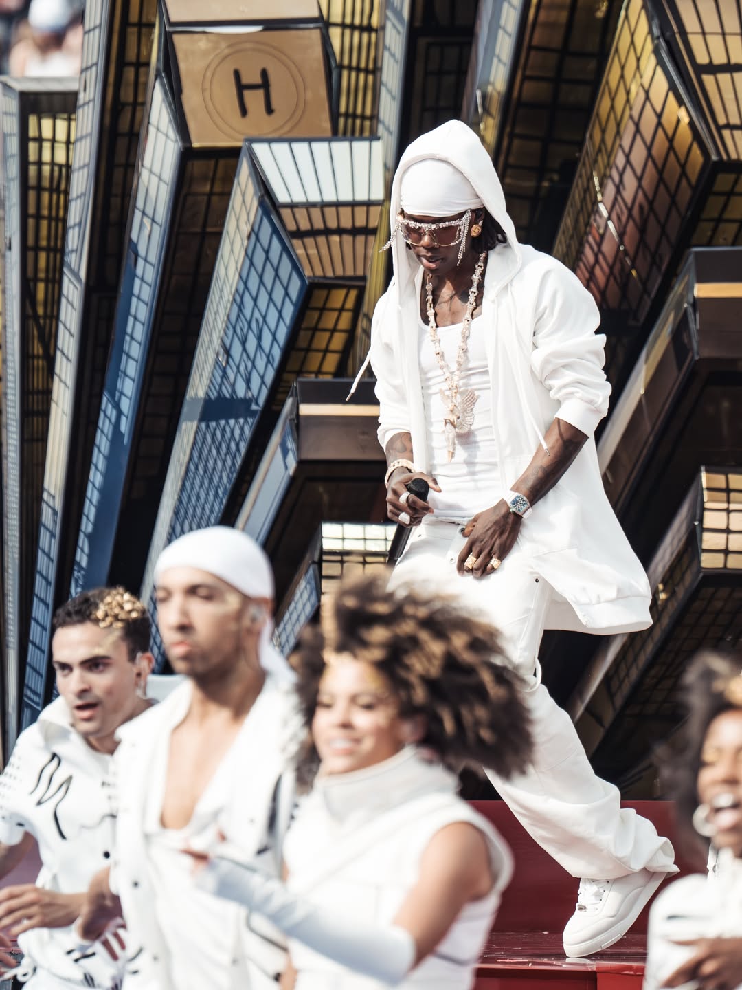 Rema walks down stage steps during his World Cup set, surrounded by backup dancers dressed in matching white clothing.
