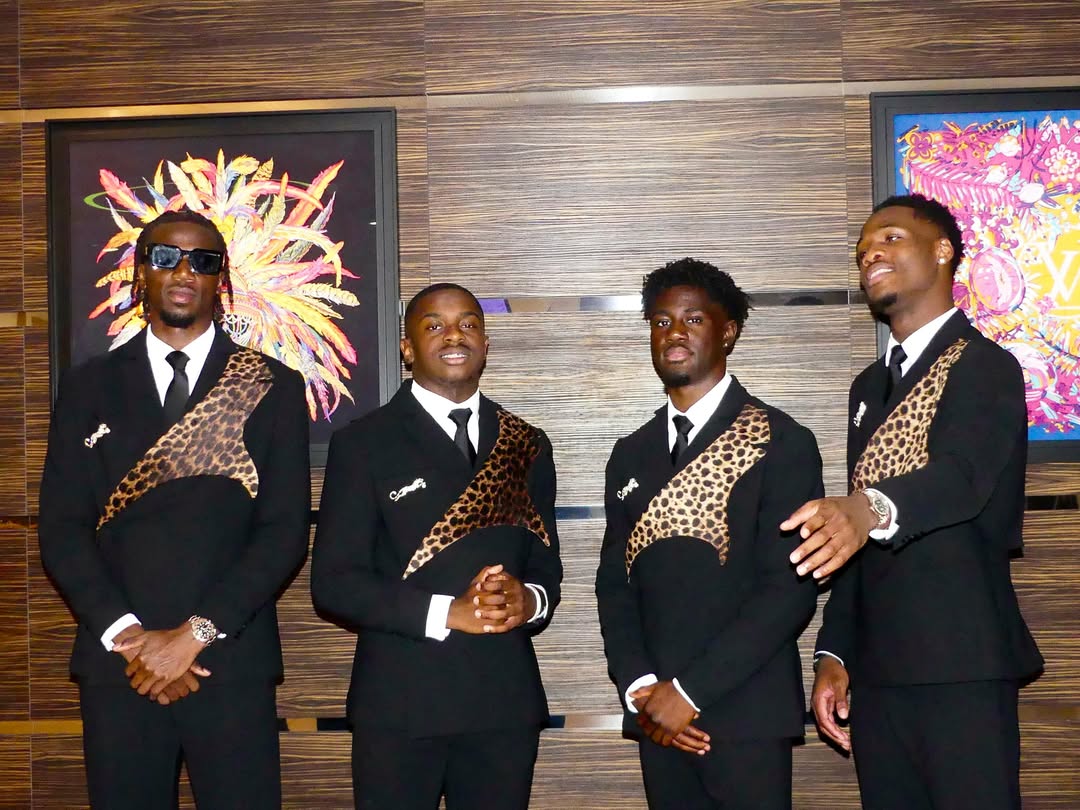 Four DR Congo players standing indoors in matching black-tie suits with leopard details and dark sunglasses.