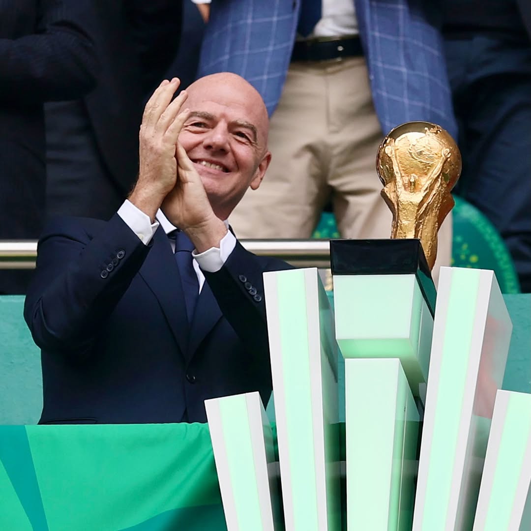 FIFA President Gianni Infantino smiling and applauding next to the official FIFA World Cup trophy at Estadio Azteca.