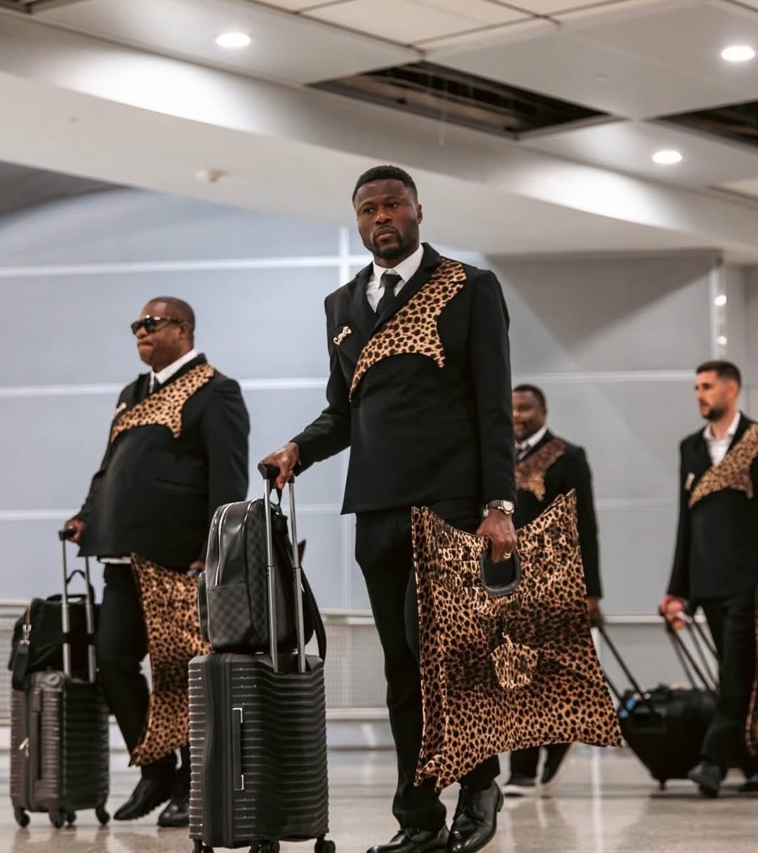 DR Congo team members walking through an airport terminal with luggage and matching leopard-print statement tote bags.
