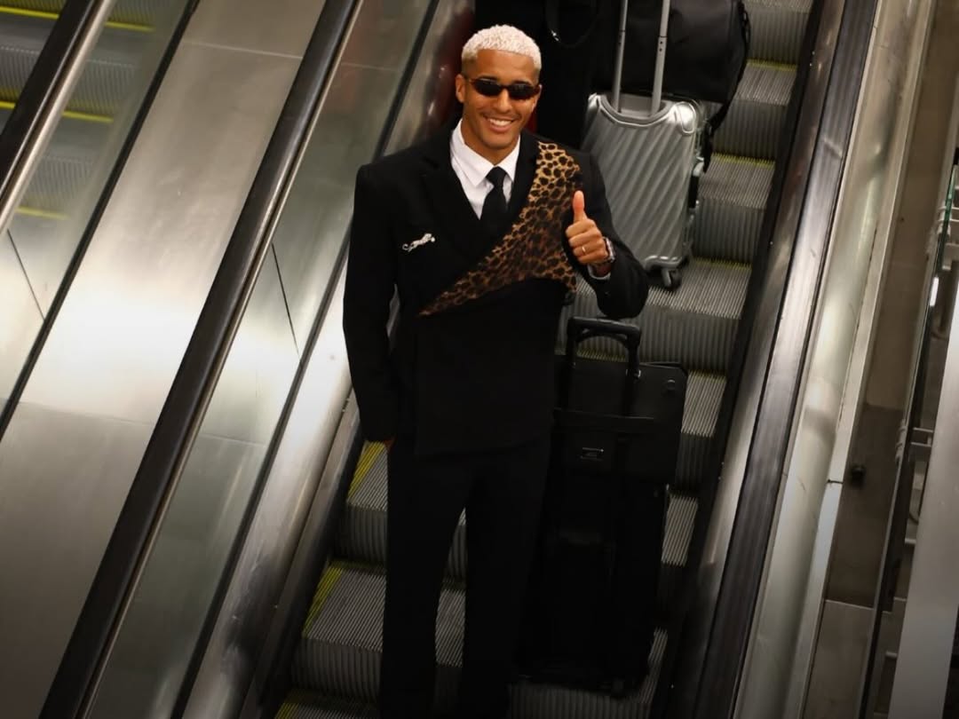 DR Congo football player on an escalator in a custom black suit with an asymmetric leopard-print panel for the 2026 World Cup.